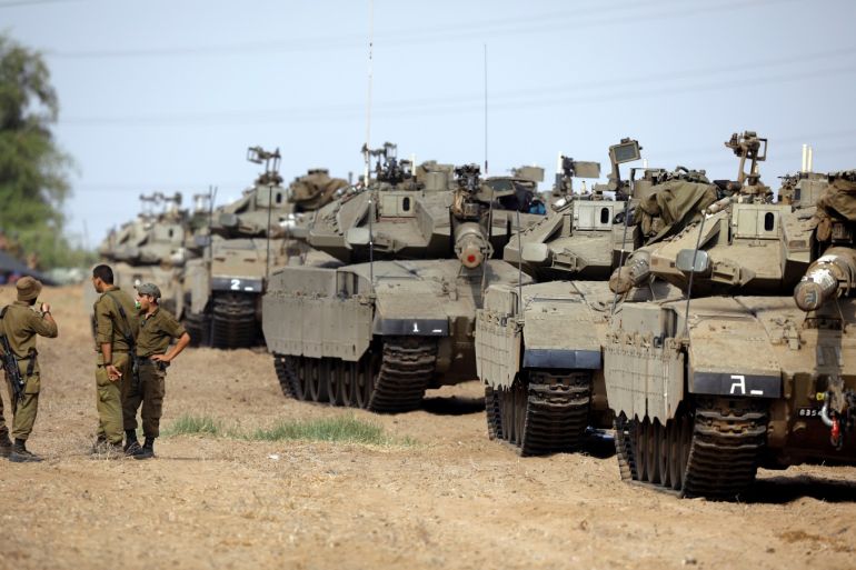 Israeli soldiers speak next to tanks as military armoured vehicles gather in an open area near