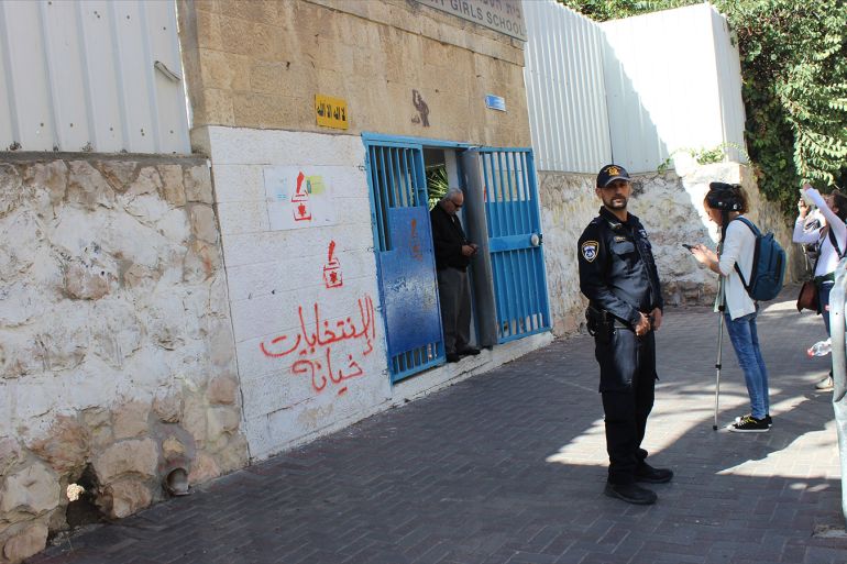 شرطي إسرائيلي يقف أمام أحد مراكز الاقتراع في القدس الشرقية وكتب على الجدار خلفه الانتخابات خيانة(الجزيرة نت).