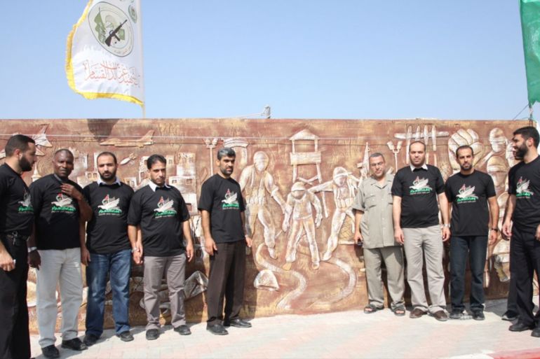 عدد من المحررين بجانب أحد أجزاء الجدارية يظهر فيها عملية اسر شاليط