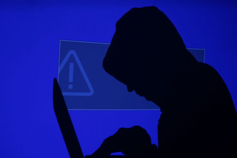 A hooded man holds a laptop computer as blue screen with an exclamation mark is projected on him in this illustration picture taken on May 13, 2017. Capitalizing on spying tools believed to have been developed by the U.S. National Security Agency, hackers staged a cyber assault with a self-spreading malware that has infected tens of thousands of computers in nearly 100 countries. REUTERS/Kacper Pempel/Illustration