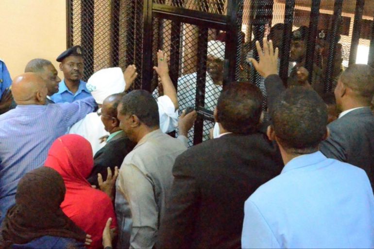 epa07780606 Sudan's ousted president Omar Hassan al-Bashir (C, in white) greets his relatives and supporters as he stands in a cage for his trial at a courtroom in Khartoum, Sudan, 19 August 2019. Al-Bashir was ousted on 11 April after months of protests and some 30 years in power. According to local media reports, al-Bashir returned to court on 19 August to answer for corruption charges. The trial resumed two days after the military council and the opposition signed a