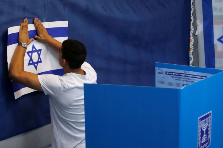 A man hangs up an Israeli flag at a polling station as Israelis begin to vote in a parliamentary election in Rosh Ha'ayin, Israel September 17, 2019. REUTERS/Ronen Zvulun
