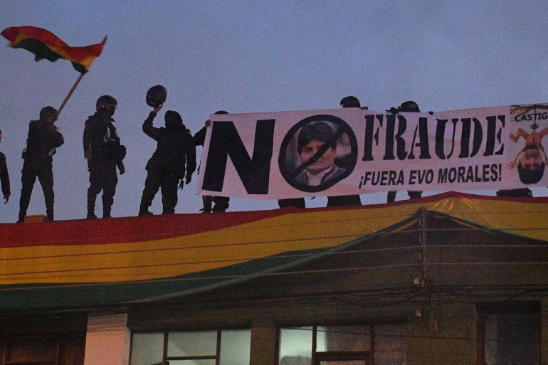 epa07982480 Bolivian police officers display a billboard that reads: 'No fraud. Out Evo Morales' from the roof of a police station in Cochabamba, Bolivia, 08 November 2019. A group of Bolivian police took control of a police station in protest against Bolivian President Evo Morales. Bolivia is immersed in a political crisis stemming from accusations by opposition and civic organizations that longtime incumbent President Evo Morales' latest election victory was tainted by fraud. EPA-EFE/Jorge Abrego