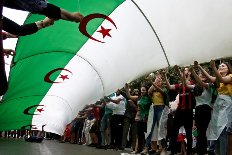 Demonstrators hold a national flag during a protest demanding the removal of the ruling elite in Algiers Algeria July 12 2019 REUTERS Ramzi Boudina.png
