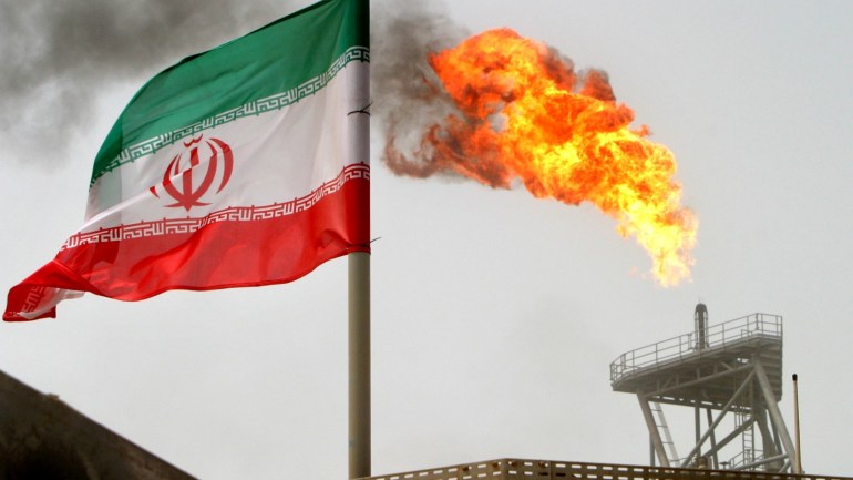 A gas flare on an oil production platform in the Soroush oil fields is seen alongside an Iranian flag in the Persian Gulf, Iran, July 25, 2005. To match Exclusive OPEC-OIL/ REUTERS/Raheb Homavandi/File Photo