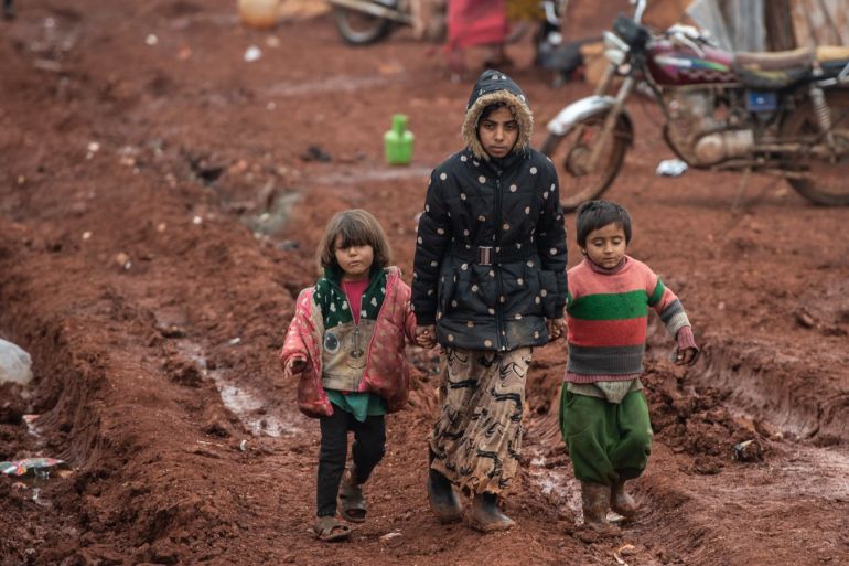 Displaced Syrian children walk on mud at Marabune camp on February 21, 2020 in Idlib