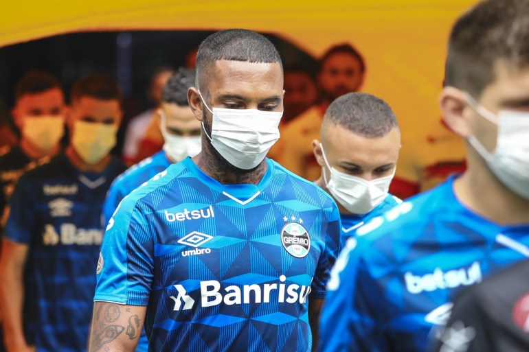 PORTO ALEGRE, BRAZIL - MARCH 15: Players of Gremio enter the field wearing masks before the match between Gremio and Sao Luiz as part of the Rio Grande do Sul State Championship 2020, to be played behind closed doors at Arena do Gremio Stadium, on March 15, 2020 in Porto Alegre, Brazil. The Government of the State of Rio Grande do Sul issued a list of new guidelines to help prevent the spread of the Coronavirus which included games played with closed doors and no public. According to the Ministry of Health, as of Saturday, March 14, Brazil had 121 confirmed cases of coronavirus. (Photo by Lucas Uebel/Getty Images)