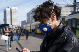 BERLIN, GERMANY - MARCH 16: A young man visiting from Brazil and wearing a protective face mask against the coronavirus checks his smartphone while walking across Alexanderplatz on March 16, 2020 in Berlin, Germany. Everyday life in Germany has become fundamentally altered as authorities tighten measures to stem the spread of the coronavirus. Public venues such as bars, clubs, museums, cinemas, schools, daycare centers and universities have closed. Many businesses are r