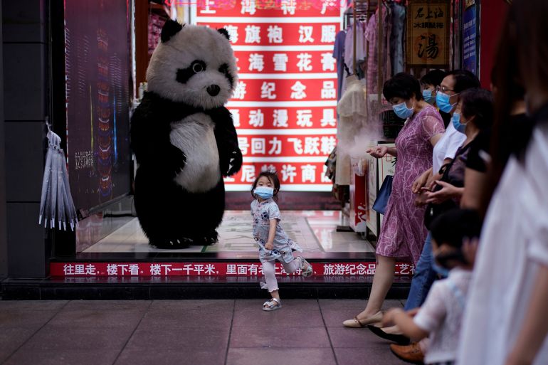 A little girl wearing face mask dances in front of a toy panda at a shopping area in Shanghai