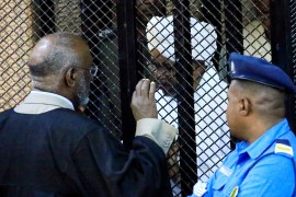 Sudan's former president Omar Hassan al-Bashir speaks to a layer as he stands inside a cage during the hearing of the verdict that convicted him of corruption charges in a court in Khartoum