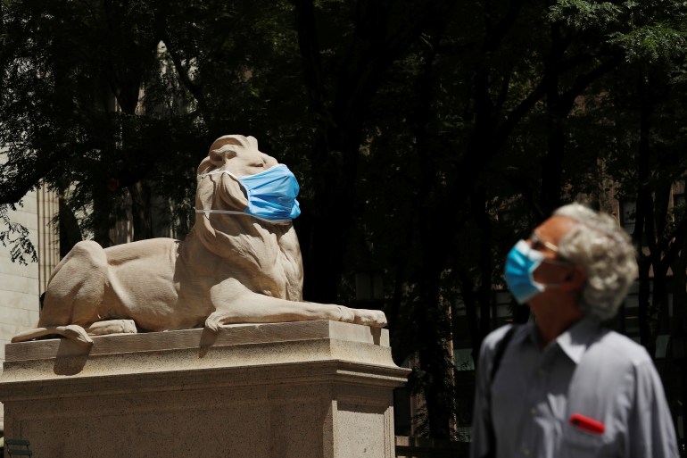 A large mask hangs on the face of a lion statue standing outside of the main branch of the New York Public Library in the Manhattan borough of New York City