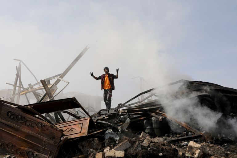 A worker reacts as he stands on the wreckage of a vehicle oil and tires store hit by Saudi-led air strikes in Sanaa