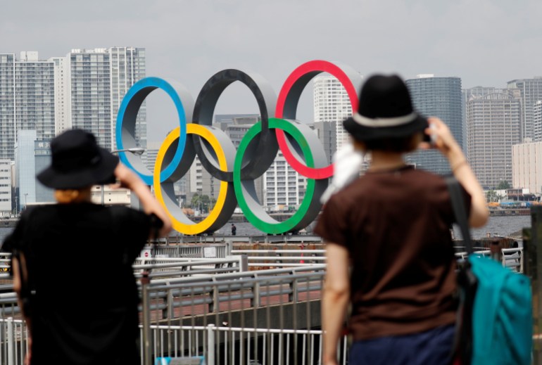 Women look at the giant Olympic rings, which are being temporarily removed for maintenance, at the waterfront area at Odaiba Marine Park in Tokyo