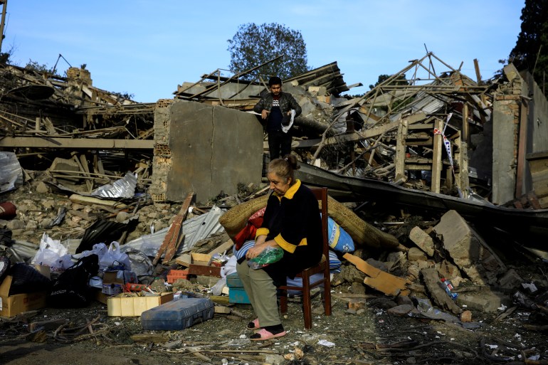 Vesile Mehmedova sits in front of debris of her brother's home as her relatives search for belongings, at a blast site hit by a rocket during the fighting over the breakaway region of Nagorno-Karabakh in the city of Ganja