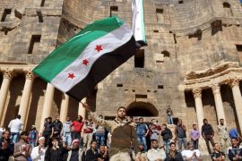 一张2016年的照片，反对派支持者在叙利亚达拉的巴士拉沙姆市一座历史悠久的剧院前挥舞着革命的旗帜 (路透)