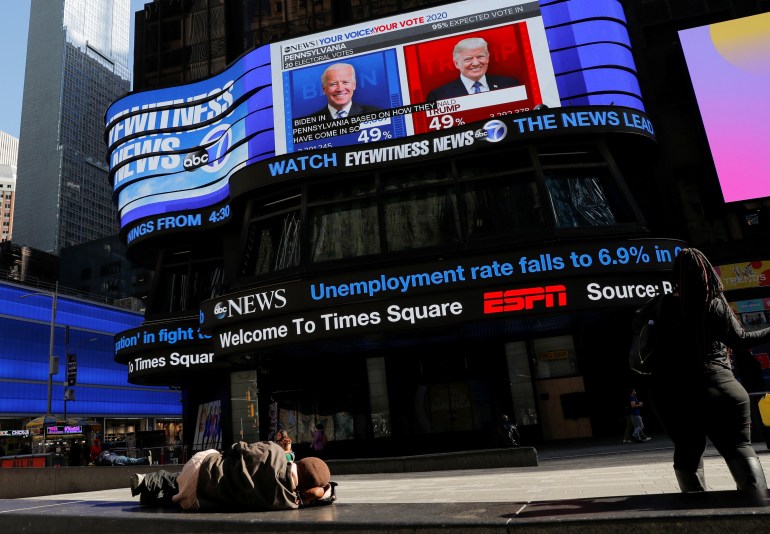 A person sleeps in front of a screen displaying election coverage in Times Square, Manhattan, New York City