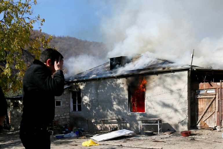 A man reacts as he stands near a house set on fire by departing Ethnic Armenians in the village of Cherektar, in the region of Nagorno-Karabakh