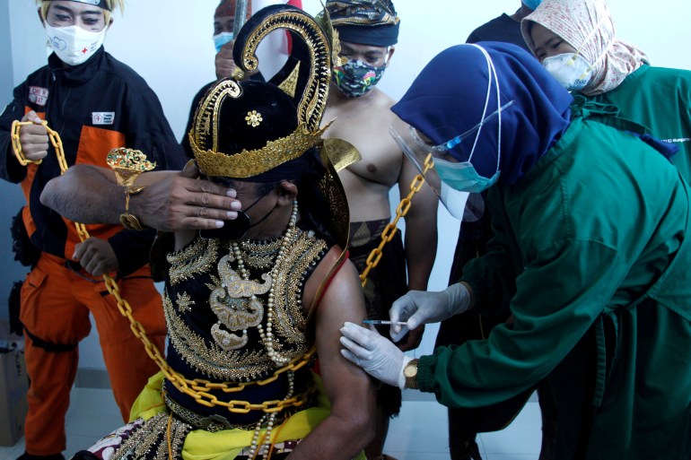 An Indonesian healthcare worker injects a dose of Sinovac's vaccine to a man dressed in Indonesia's traditional human puppet costume, as Indonesia drives mass vaccination for the coronavirus disease (COVID-19), at a hospital in Solo