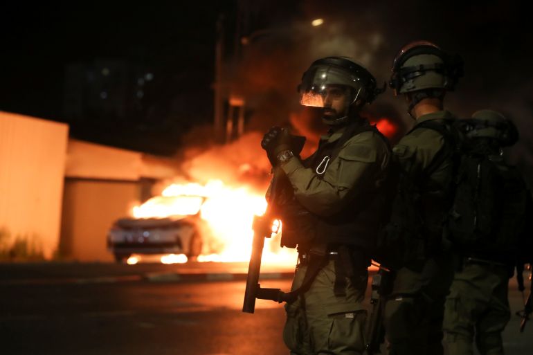 Israeli security force members stand near a burning Israeli police car during clashes between Israeli police and members of the country's Arab minority in the Arab-Jewish town of Lod