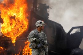 2010年7月23日，阿富汗坎大哈北部的阿尔甘达卜山谷内，一名美国士兵站在一辆燃烧着的装甲车旁边，在此之前，这辆装甲车撞上了一个简易爆炸装置 (路透社)