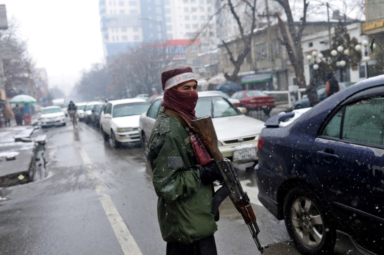 A Taliban fighter stands guard at a checkpoint during a snowfall in Kabul