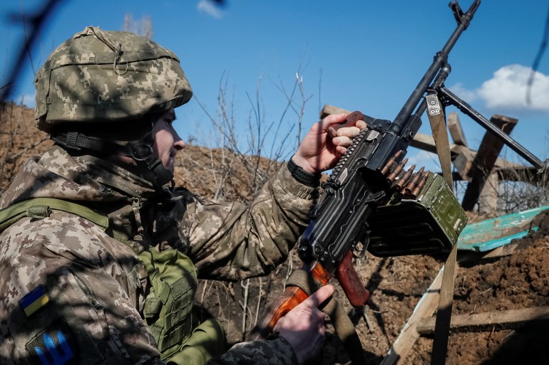 Ukrainian service member holds a machine gun in a trench on the front line near the village of Travneve
